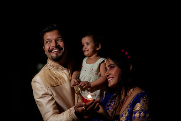 Young and beautiful Indian Gujarati father,mother and kid in traditional dress celebrating Diwali with diya/lamps on the terrace in darness  on Diwali evening. Indian lifestyle and Diwali celebration