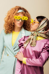 african american girl and redhead woman in sunglasses with flowers isolated on beige