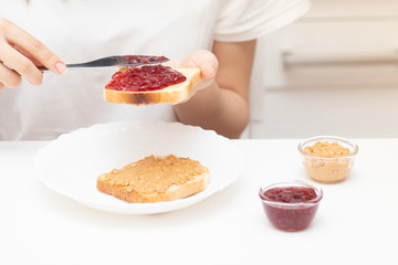 Female hands spread raspberry jam on bread, prepare sandwiches in the morning at home for breakfast...