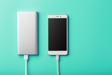 Power Bank charges your smartphone on a blue background. Universal external battery for gadgets free space and minimalistic composition.