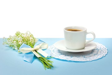 cup of black coffee on a saucer and a bouquet of lily of the valley flowers on a white background with copy space
