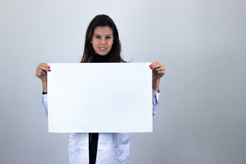 Portrait of happy pretty  middle age woman smiling holding a big white placard, sign copy space, isolated on gray background studio shot in white coat uniform, dark air. Place for your text in copy sp