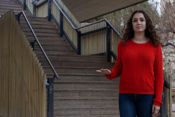 pretty caucasian young woman copyspace imaginary on palm to insert advertisment, in the park, orange sweater and jeans, long curly hair. Place for your text in copy space.