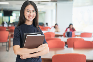 Obraz premium Back to school education knowledge college university concept, Beautiful female college student holding her books smiling happily standing in library, Learning and education concept