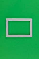 White photo frame on medium green paper background for Spring, Easter, St Patrick, Daylight Saving Time.  Flay lay, top view, copy space.