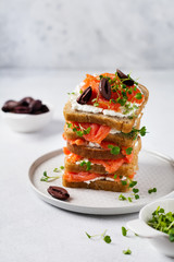 Sandwiches with smoked pink salmon olives, kalamata, microgreens and cream cheese on gray ceramic plate and trendy concrete background. Traditional Scandinavian toast. Top view.