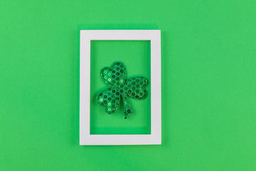 White photo frame on medium green paper background for Spring, St Patrick's Day  Flay lay, top view, copy space.