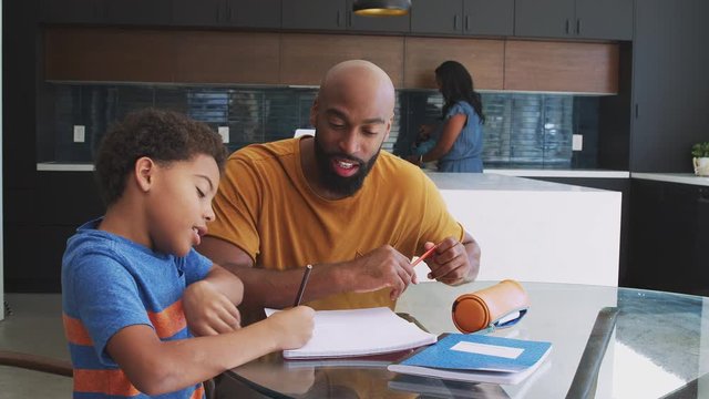 African American Parents Helping Son Studying Homework In Kitchen