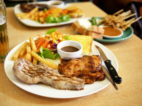 Grilled steaks and New Orleans Chicken Wings ,Pork satay with vegetables on a white plate on a wood table Blurred image