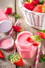 Strawberry milkshake in bottles, with fresh strawberries and mint on sunlight summer wooden and glass background, copy space