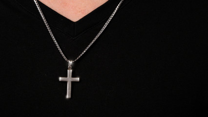 Silver crucifix or cross pendant and necklace on body or hand studio shot black color background...