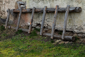 The rural or village landcape with a grey ladder or staircase leaned on the old stone building wall with the ground covered with green grass