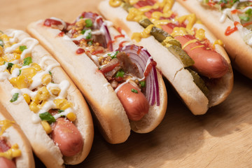 various delicious hot dogs with vegetables and sauces on wooden table