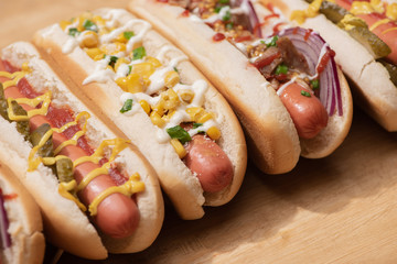 various delicious hot dogs with vegetables and sauces on wooden table