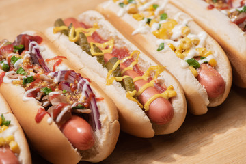 various delicious hot dogs with vegetables and sauces on wooden table