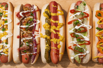 top view of various delicious hot dogs with vegetables and sauces on wooden table