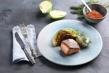 Fish and seafood cuisine. Red fish with fried cabbage, sauce and red caviar on a blue plate. Background image, copy space
