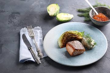Fish and seafood cuisine. Red fish with fried cabbage, sauce and red caviar on a blue plate. Background image, copy space