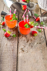 Red summer drink with ice, cold strawberry mojito or lemonade with fresh strawberries and mint on sunlight summer wooden and glass background, copy space