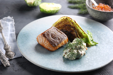 Fish and seafood cuisine. Red fish with fried cabbage, sauce and red caviar on a blue plate. Background image, copy space