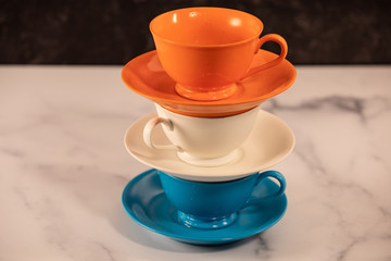 Stacked ceramic orange white and bright blue tea and coffee mugs with saucers piled up