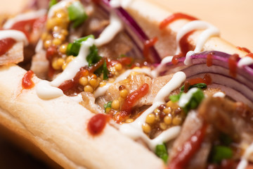 close up view of delicious hot dog with red onion, bacon and Dijon mustard