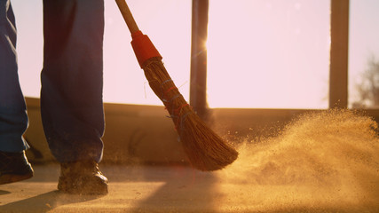 LOW ANGLE: Contractor sweeping the dirty floor with a straw broom at sunset. - obrazy, fototapety, plakaty