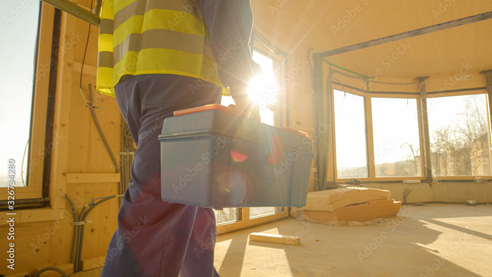 Wall mural CLOSE UP: Golden sunbeams shine on worker coming to work in prefabricated house.