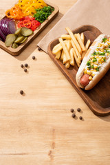delicious hot dog near board with sliced vegetable and french fries on wooden table