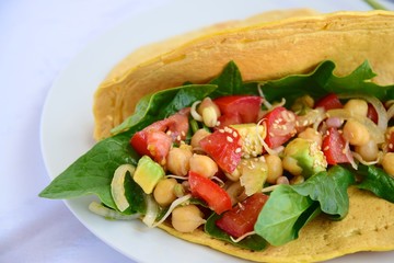 Chickpea flour tortilla wraps filled with spinach, tomato, avocado, onion and sesame seeds