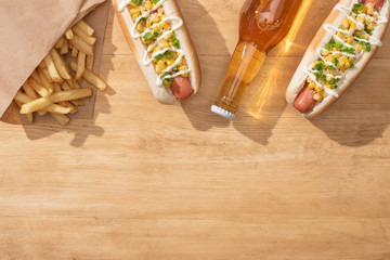 top view of delicious hot dogs with corn, green onion and mayonnaise near french fries and beer on wooden table