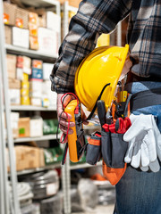 Electrician holds multimeter tester in hand, helmet with protective goggles. Construction industry,...