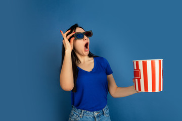 Emotional watching cinema. Beautiful caucasian woman's portrait on blue studio background. Beautiful female brunette model. Concept of human emotions, facial expression, sales, ad, copyspace.