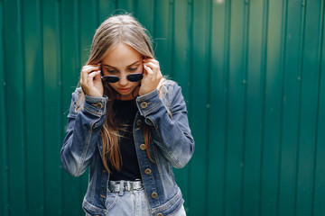 young pretty attractive girl in denim clothes in glasses on a simple dark green background with place for text.