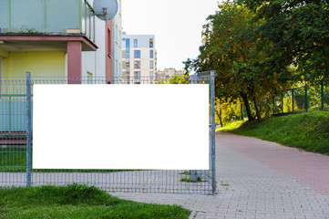 Blank white banner for advertisement on the fence. Residential area on a sunny summer day.
