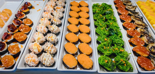 Rows of japanese sushi food. Maki ands rolls with tuna, salmon, shrimp, crab and avocado. Top view of assorted sushi in black plastic container being sale at market. Selective focus.