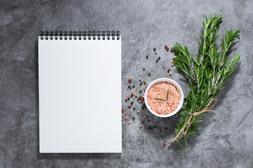 Blank white notepad and set of aromatic spices and herbs on dark stone table with. recipe book or restaurant menu template.