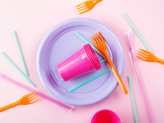 Disposable colorful plastic dishes, cutlery, straws and glasses. Creative Flat lay