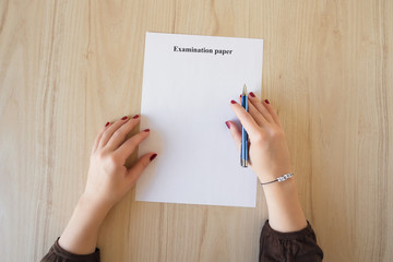 Obraz premium Student girl hand with bracelet and love word. Empty examination paper sheet on the table. First love during university exam. Concept