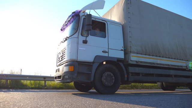 Truck driving on a highway. Lorry rides through the countryside with sunset at background. Bottom Side view Slow motion Close up
