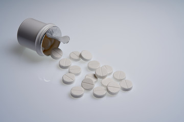 White tablets are scattered from a bottle on a gray background. Pharmaceutical business concept.