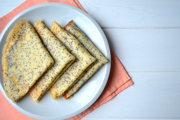 Thin pancakes with poppy seeds folded in triangles on a white plate. Traditional food for Maslenitsa.