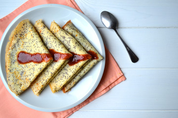 Traditional Russian and Ukrainian this pancakes with poppy seeds and strawberry jam on a white plate. National food for Maslenitsa.