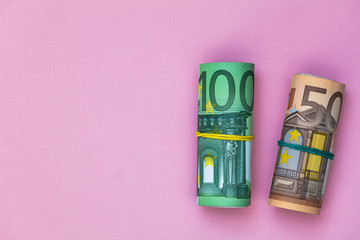 rolls of  50 and 100 euro banknotes on pink background