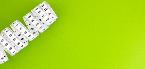 Unfolded white tape measure, White measuring tape isolated on green background. Close the tailor measuring tape on a green background. The concept of sports, diet, fitness, healthy eating. Copy space
