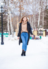 Fototapeta na wymiar Full-length portrait of a young woman in black long down jacket posing in winter park