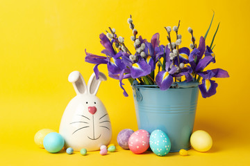 Bunny, Easter eggs and bucket with flowers on yellow background