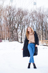 Full-length portrait of a young woman in black long down jacket posing in winter park