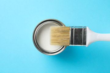Paint can and brush on blue background, top view