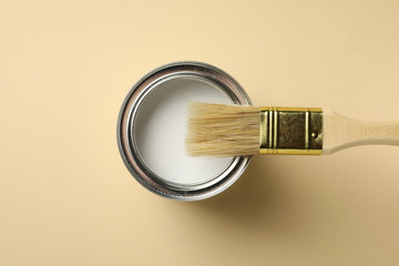 Paint can and brush on beige background, top view